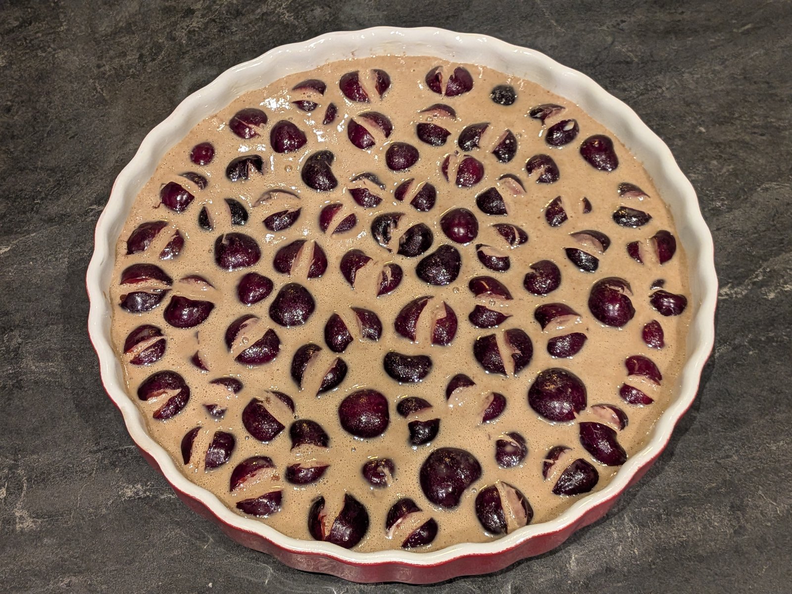 Appareil à clafoutis (œufs, lait, skyr, purée d'amande) versé sur les cerises avant cuisson